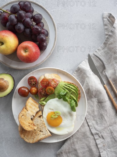 Enjoying a nutritious and delicious breakfast with whole wheat toast topped with avocado, a fried egg, and a side of fresh fruits