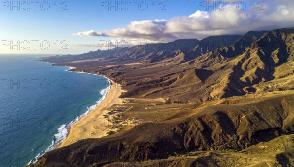 Desert landscape converges with ocean along a rugged coastal area, shore break at cliffs, blue cloudy sky at sunset, dry landscape in an aerial drone view, AI generated