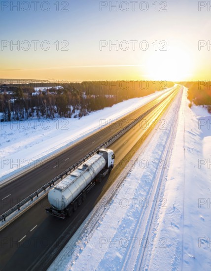 Petrol cargo truck lorry tanker driving on highway hauling oil products at sunrise, wide snowy landscape in winter, AI generated