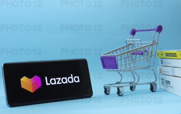 Dhaka, Bangladesh- 03 July 2025: Smartphone with Lazada logo next to a small shopping cart and boxes against a blue background