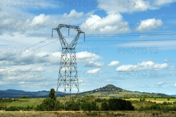 High voltage power lines against a bright blue sky with scattered clouds, Puy de Dome, Auvergne Rhone Alpes, France