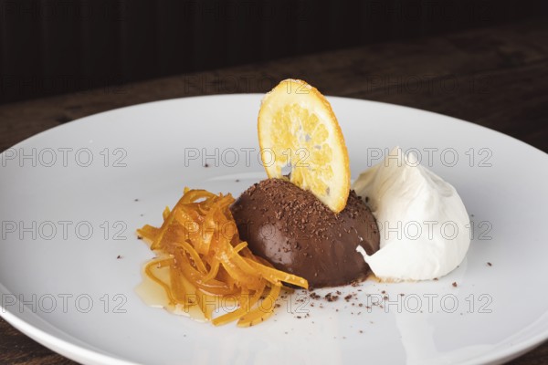 Chocolate mousse dessert with candied orange peel, dried orange slice, and cream on a white plate