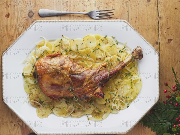 Whole roast leg of lamb with thinly sliced potatoes, onions, and fresh thyme sprigs