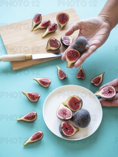Hands arranging fresh, cut figs on a white plate and cutting board