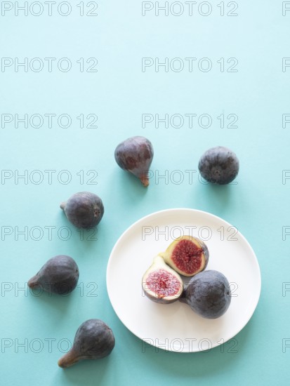 Ripe figs arranged on a white plate and scattered on a blue surface