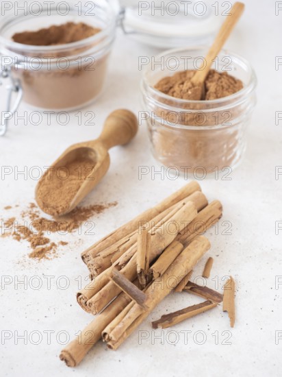 Cinnamon sticks and ground powder in jars with a scoop on a white background