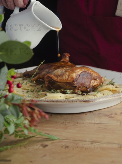 Hand pouring gravy from a pitcher onto a roasted lamb leg