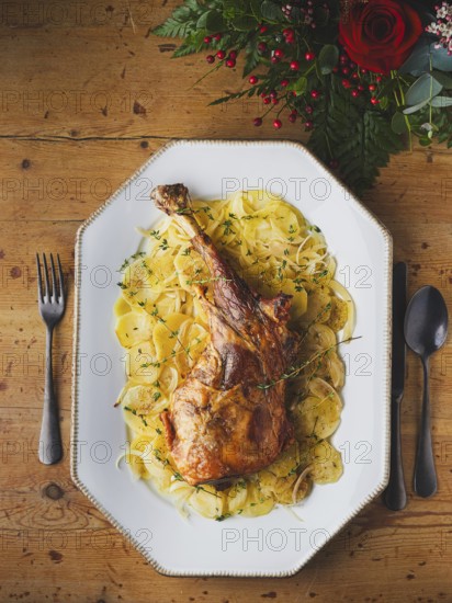 Roasted leg of lamb serving with sliced potatoes and fresh thyme on a wooden table