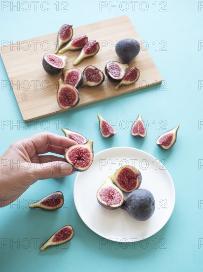 Hand holding fresh cut fig over a plate with more figs