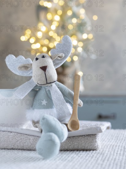 Fabric reindeer toy sitting with a wooden spoon and cozy christmas lights
