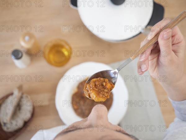 Woman holding a spoonful of lentil stew at lunch, top view of the table