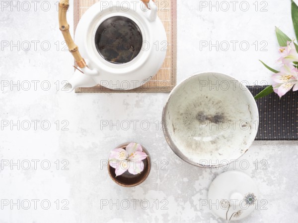White teapot with bamboo handle, empty bowl, lid and pink flowers on light textured background are ready for tea ceremony