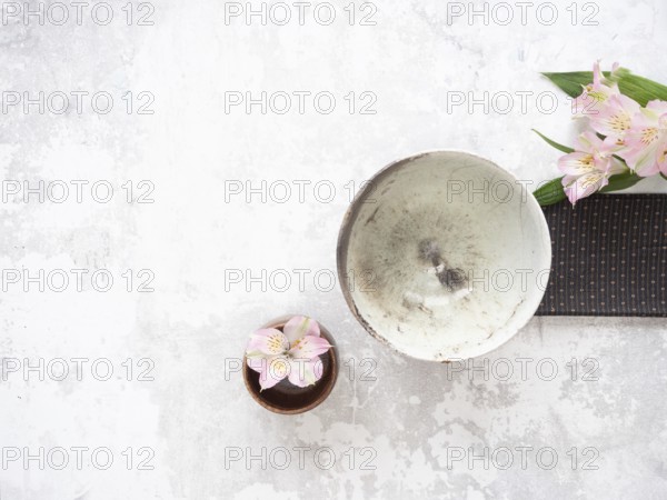 Empty ceramic bowl, pink alstroemeria flowers, and brown placemat creating a minimalist arrangement on textured surface, ideal for food photography or wellness blogs