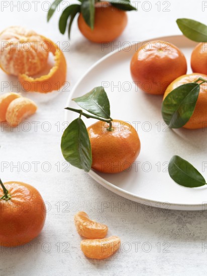 Vibrant tangerines with green leaves, showcasing freshness and citrusy appeal on a white plate and table