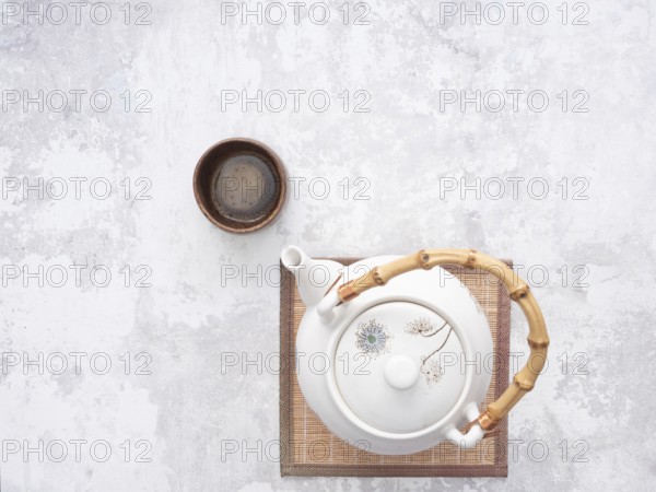 White teapot with bamboo handle and small wooden teacup on bamboo mat, ready for traditional asian tea ceremony