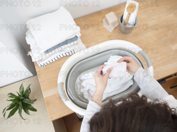 Woman putting clean white clothes into laundry basket, preparing for drying