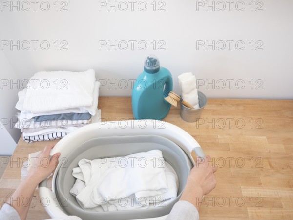 Woman holding laundry basket with clean white clothes, getting ready to do laundry with detergent and stain remover