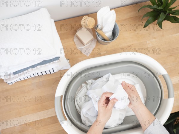 Woman soaking white clothes in bucket using natural soap and brush, promoting sustainable laundry practices