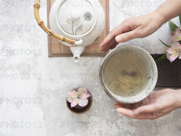 Woman gently holding a tea bowl during a traditional japanese tea ceremony, with teapot and flower nearby