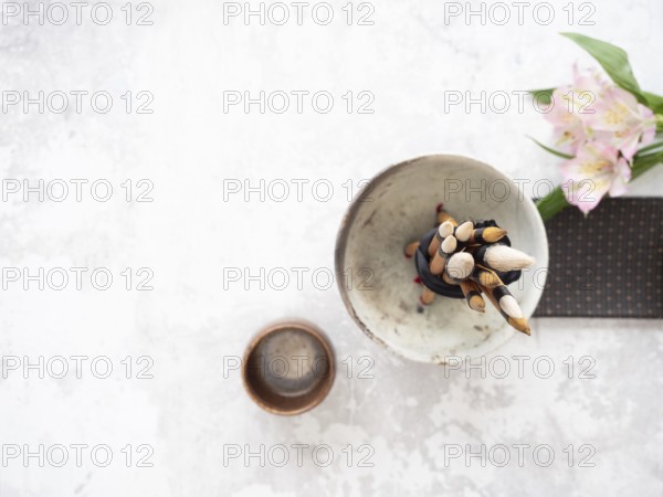 Calligraphy brushes tied with black ribbon in ceramic bowl near inkstone and pink flowers, ready for traditional writing session