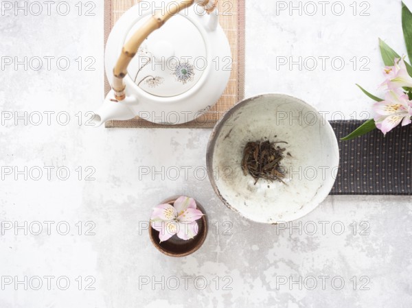Traditional tea set with teapot, teacup, dried tea leaves, and pink alstroemeria flowers creates a serene atmosphere