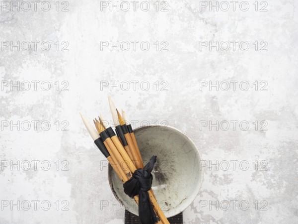 Multiple calligraphy brushes tied together with a black ribbon are resting on a ceramic bowl, evoking traditional art practices