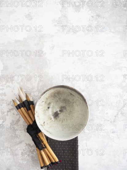 Calligraphy brushes tied with black ribbon and ceramic bowl resting on textured surface, creating artistic composition with ample copy space