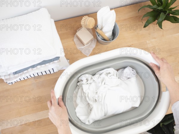 Woman soaking white laundry in a collapsible basin using natural soap, promoting sustainable and eco-conscious washing practices