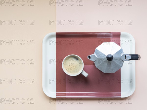 Coffee cup and moka pot sitting on a serving tray, minimalist flat lay on a pastel pink and beige background