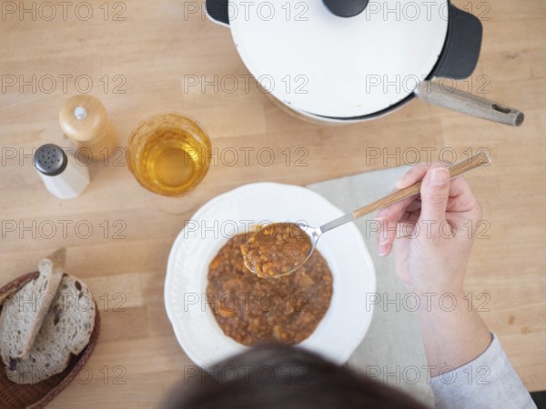 Woman holding spoon with lentil soup, enjoying a healthy meal at home with bread and a drink