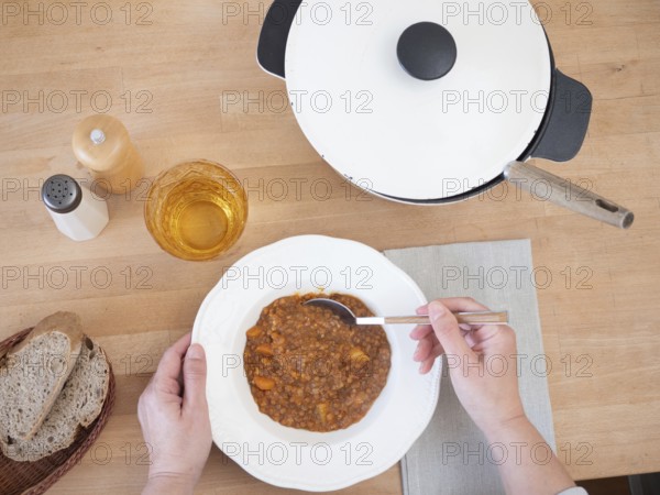 Woman enjoying a healthy and hearty lentil stew, accompanied by bread and a refreshing drink, served on a rustic wooden table