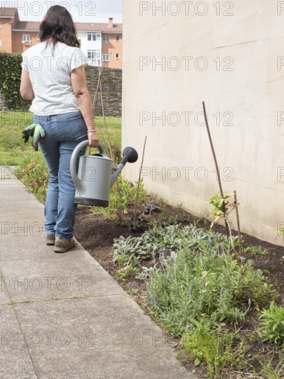 Woman is walking with a watering can to water the plants in her garden