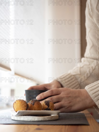 Woman enjoying a relaxing moment with coffee or tea and cookies in a cozy cafe by the window