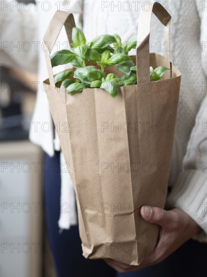 Woman holding a brown paper bag with fresh basil leaves, promoting sustainability and healthy eating