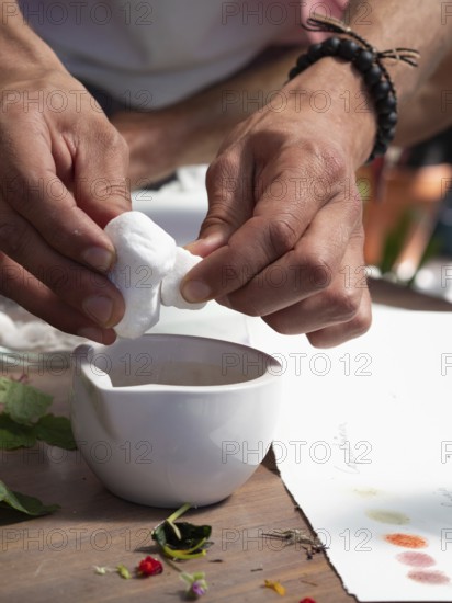 Hands squeezing white flower petals above a mortar for creating natural inks and pigments in a workshop