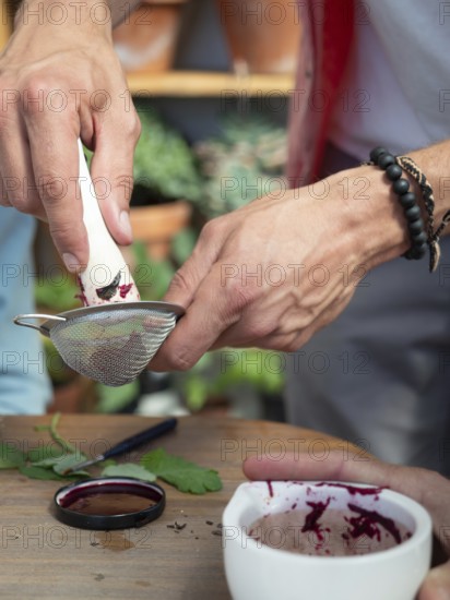 Hands filtering beetroot juice through a sieve, creating natural ink or pigment in a workshop setting