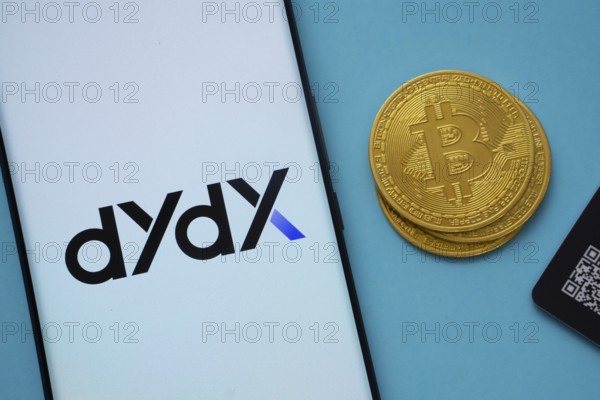 Dhaka, Bangladesh- 03 Oct 2025: Dydx logo on smartphone screen near Bitcoin coin and QR code on blue background