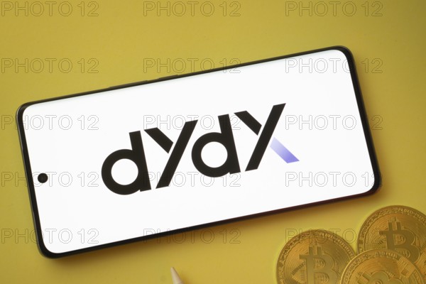 Dhaka, Bangladesh- 03 Oct 2025:Dydx logo on smartphone screen near Bitcoin coin and QR code on yellow background