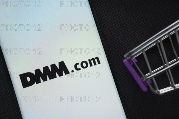 Dhaka, Bangladesh- 03 Oct 2025: A smartphone displaying the Dmm.com logo next to a miniature shopping cart on a background