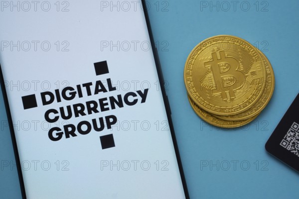 Dhaka, Bangladesh- 03 Oct 2025: Digital currency group logo on smartphone screen near Bitcoin coin and QR code on blue background