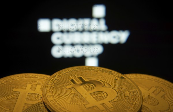 Dhaka, Bangladesh- 03 Oct 2025: Close-up of Bitcoin coins with the Digital currency group logo visible on a screen in the background