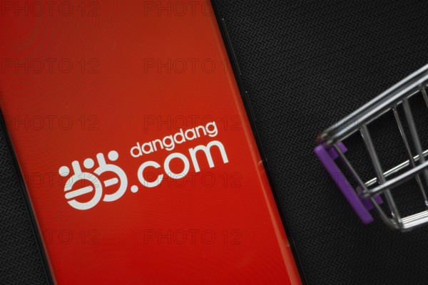 Dhaka, Bangladesh- 03 Oct 2025: A smartphone displaying the Dangdang.com logo next to a miniature shopping cart on a background