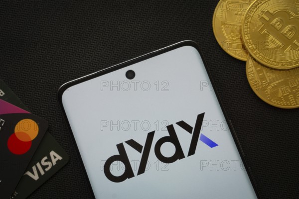 Dhaka, Bangladesh- 03 Oct 2025: Smartphone displaying Dydx logo surrounded by Bitcoin coins and payment cards