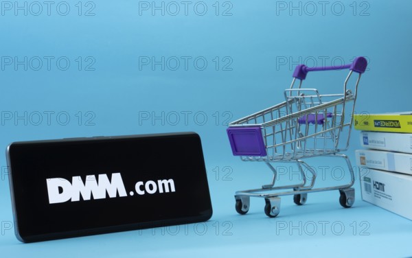 Dhaka, Bangladesh- 03 Oct 2025: Smartphone with Dmm.com logo next to a small shopping cart and boxes against a blue background