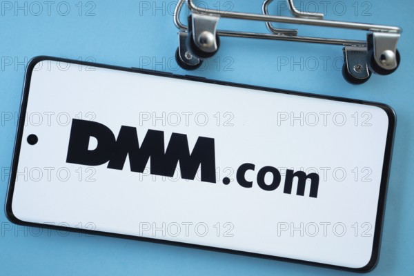 Dhaka, Bangladesh- 03 Oct 2025: Smartphone screen showing the Dmm.com logo with shopping cart wheels on a blue background