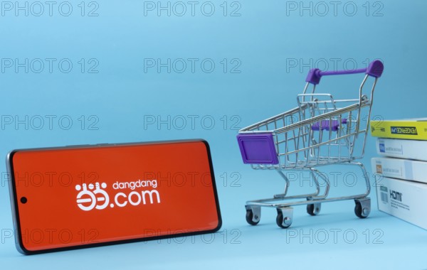 Dhaka, Bangladesh- 03 Oct 2025: Smartphone with Dangdang.com logo next to a small shopping cart and boxes against a blue background