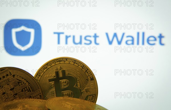 Dhaka, Bangladesh- 30 Sep 2025: Close-up of Bitcoin coins with the Trust Wallet logo visible on a screen in the background