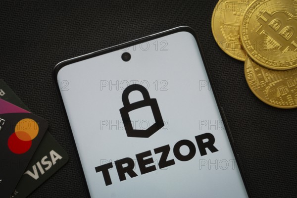 Dhaka, Bangladesh- 30 Sep 2025: Smartphone displaying Trezor logo surrounded by Bitcoin coins and payment cards