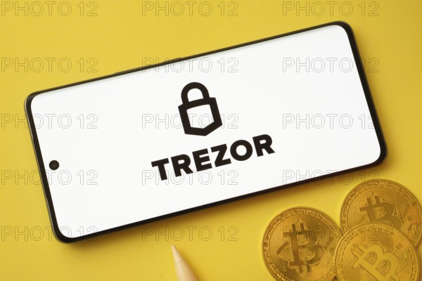 Dhaka, Bangladesh- 30 Sep 2025: Trezor logo on smartphone screen near Bitcoin coin and QR code on yellow background