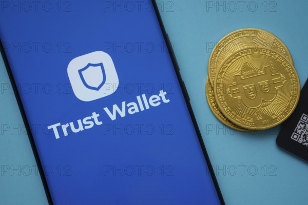 Dhaka, Bangladesh- 30 Sep 2025: Trust Wallet logo on smartphone screen near Bitcoin coin and QR code on blue background